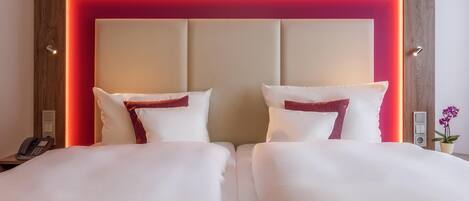 Habitación de hotel con una cama grande, dos almohadas, un cabecero de madera y una tira de luz roja.