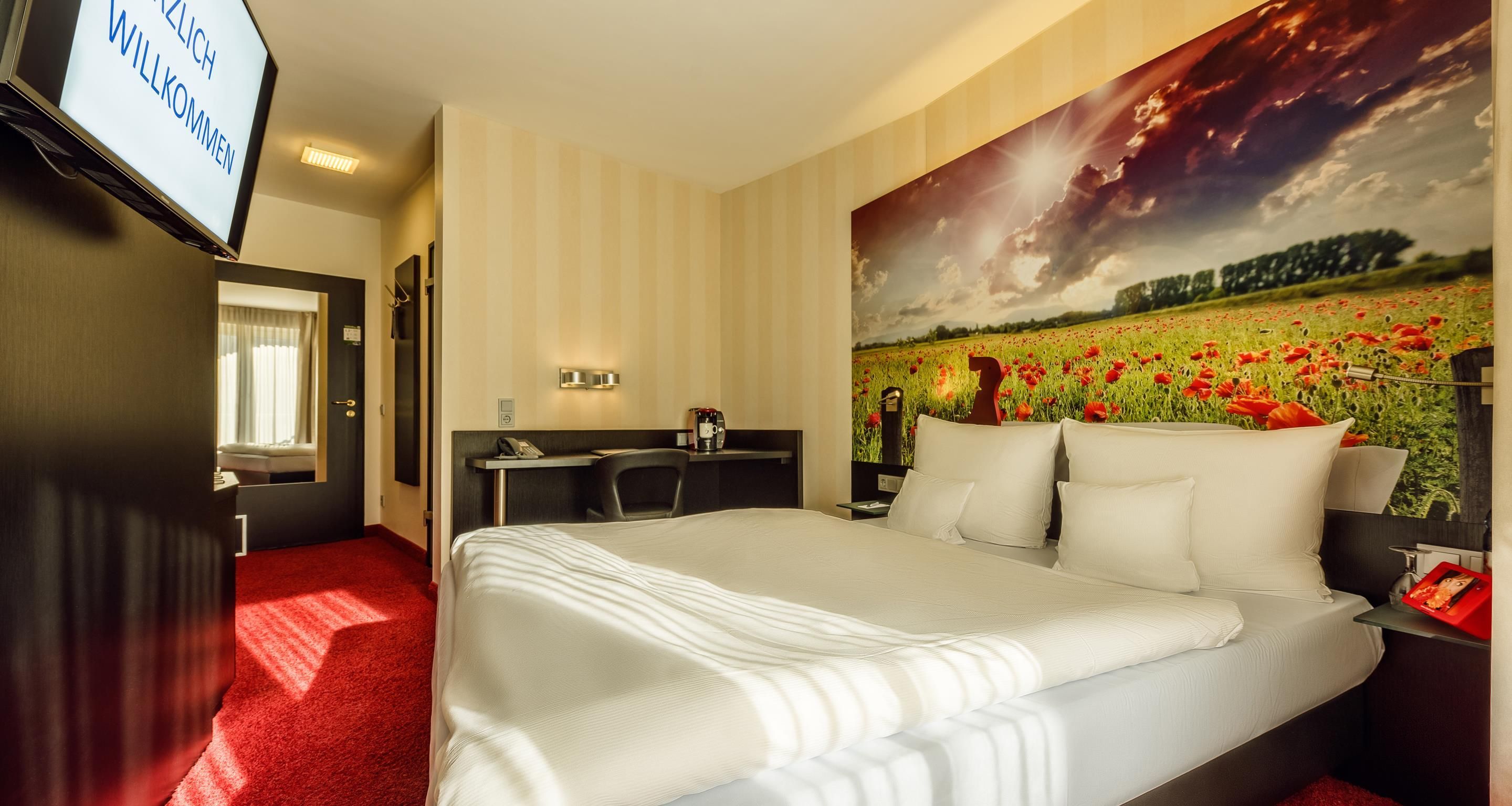 Habitación de hotel con cama, escritorio, silla, teléfono y un mural grande en la pared.
