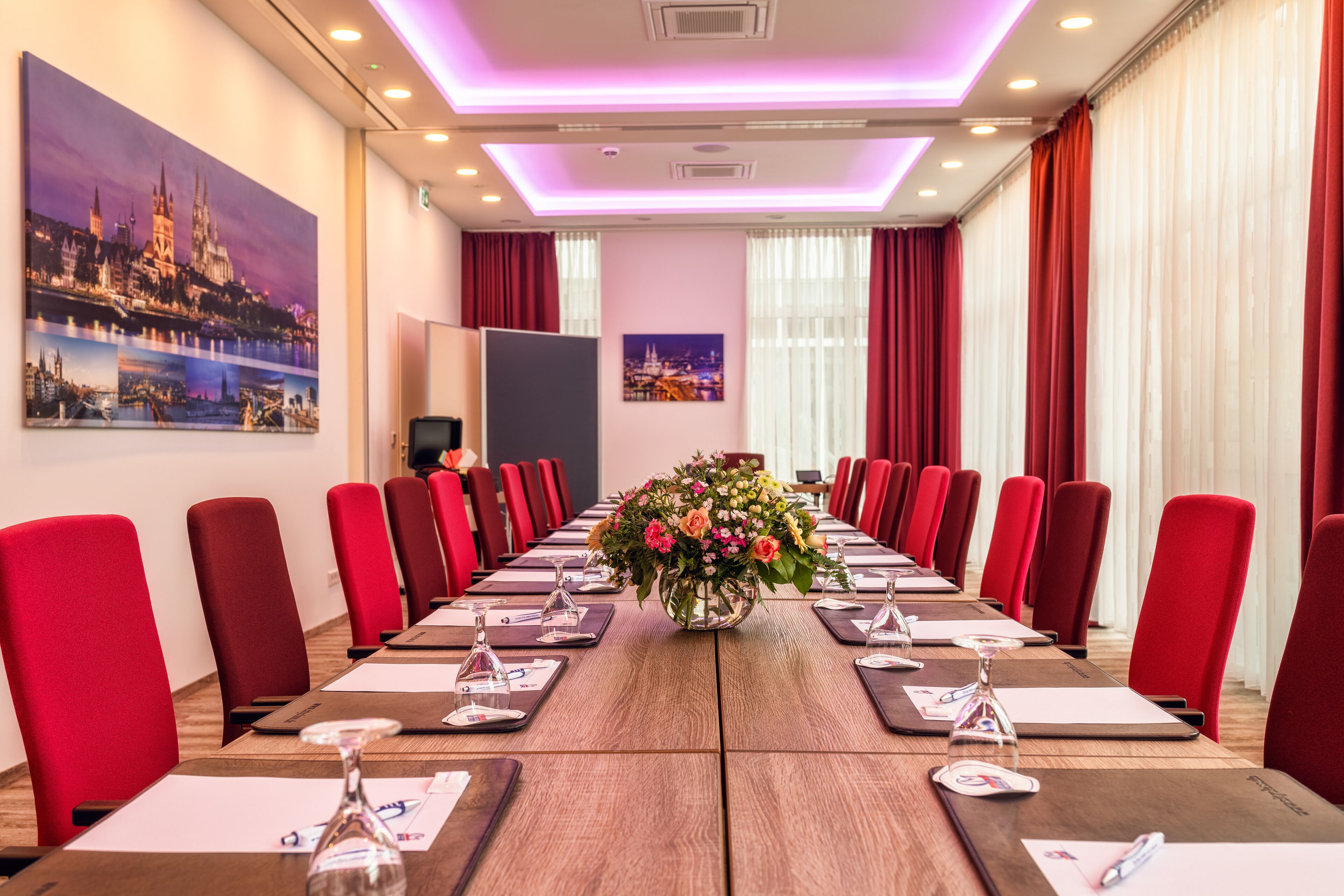 Une salle de conférence avec une longue table, des chaises rouges et un arrangement floral au centre.