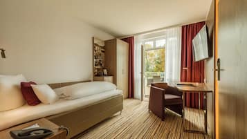 Quarto de hotel com sofá-cama, escrivaninha com cadeira, televisão e uma grande janela com cortinas.