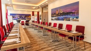 A conference room with a long table, red chairs, and a cityscape painting on the wall.