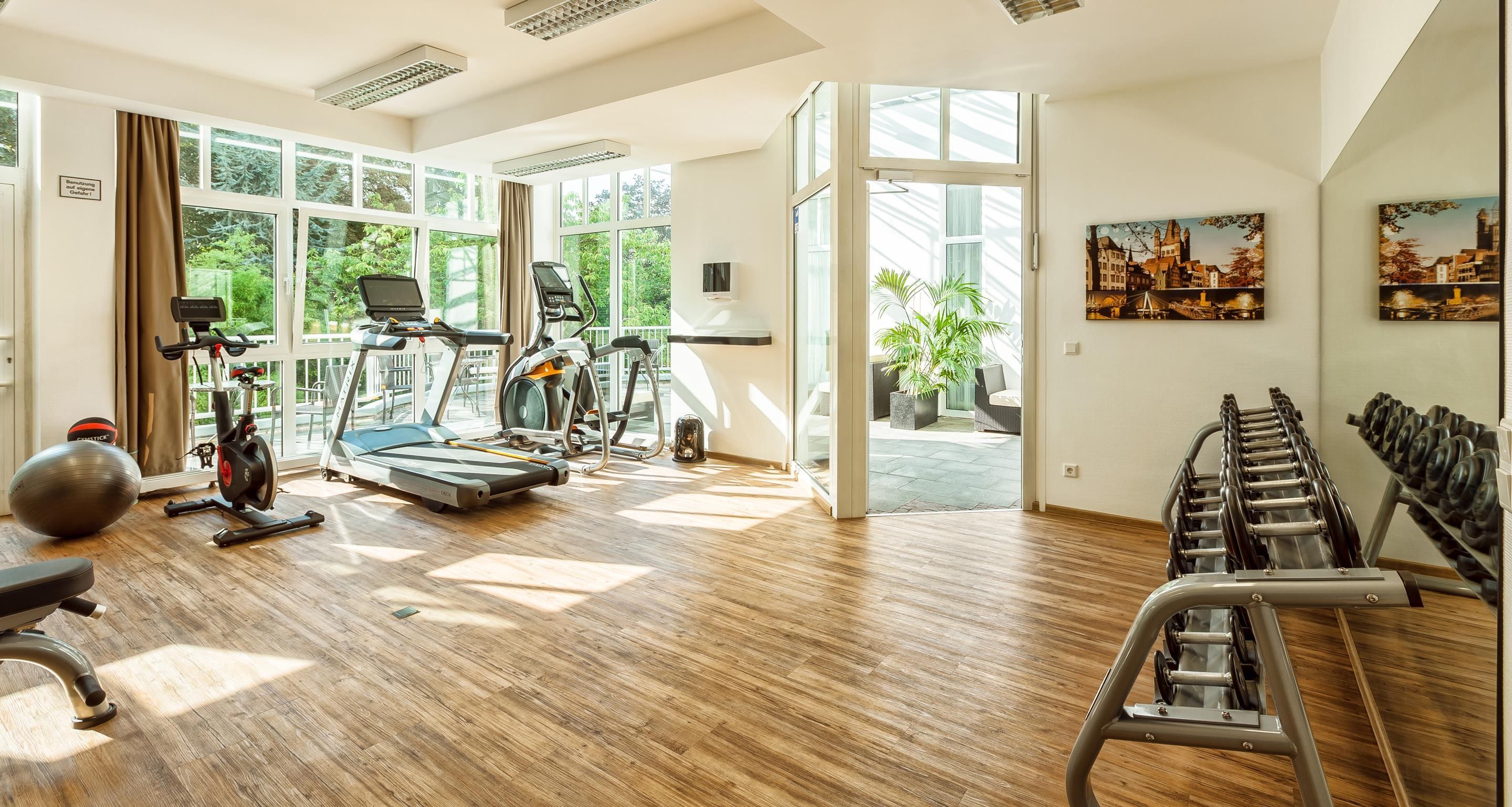Ein großzügiger Fitnessraum mit diversen Trainingsgeräten, großen Fenstern und Blick auf Grünflächen.