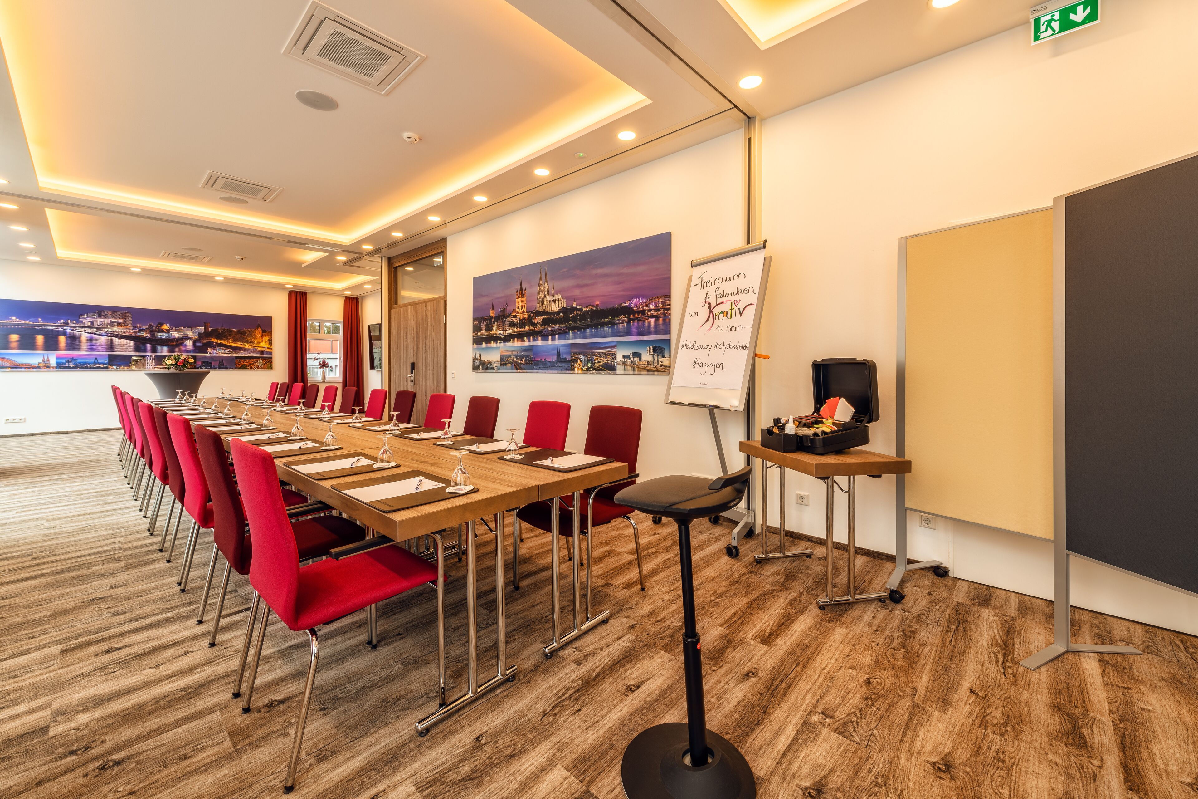 A conference room with a long table, red chairs, a whiteboard, and a cityscape painting on the wall.
