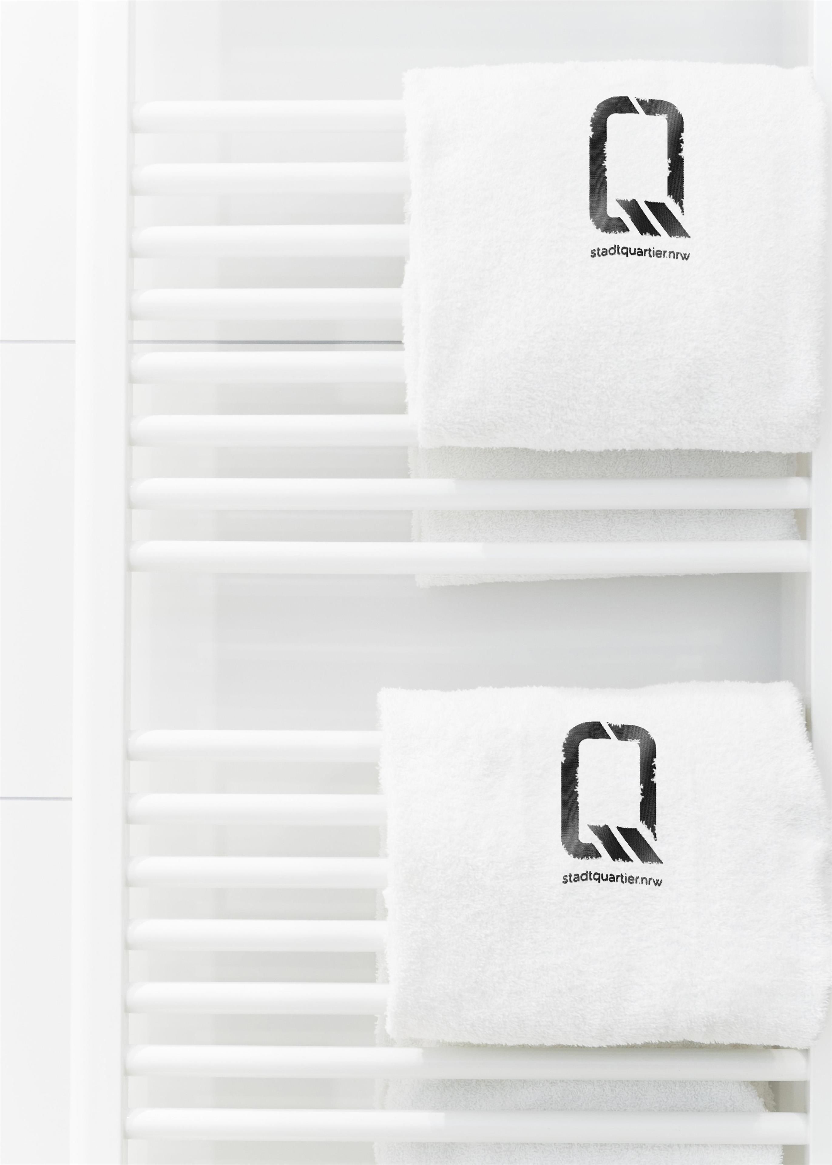 A white towel rack with two towels, each featuring a logo and text.