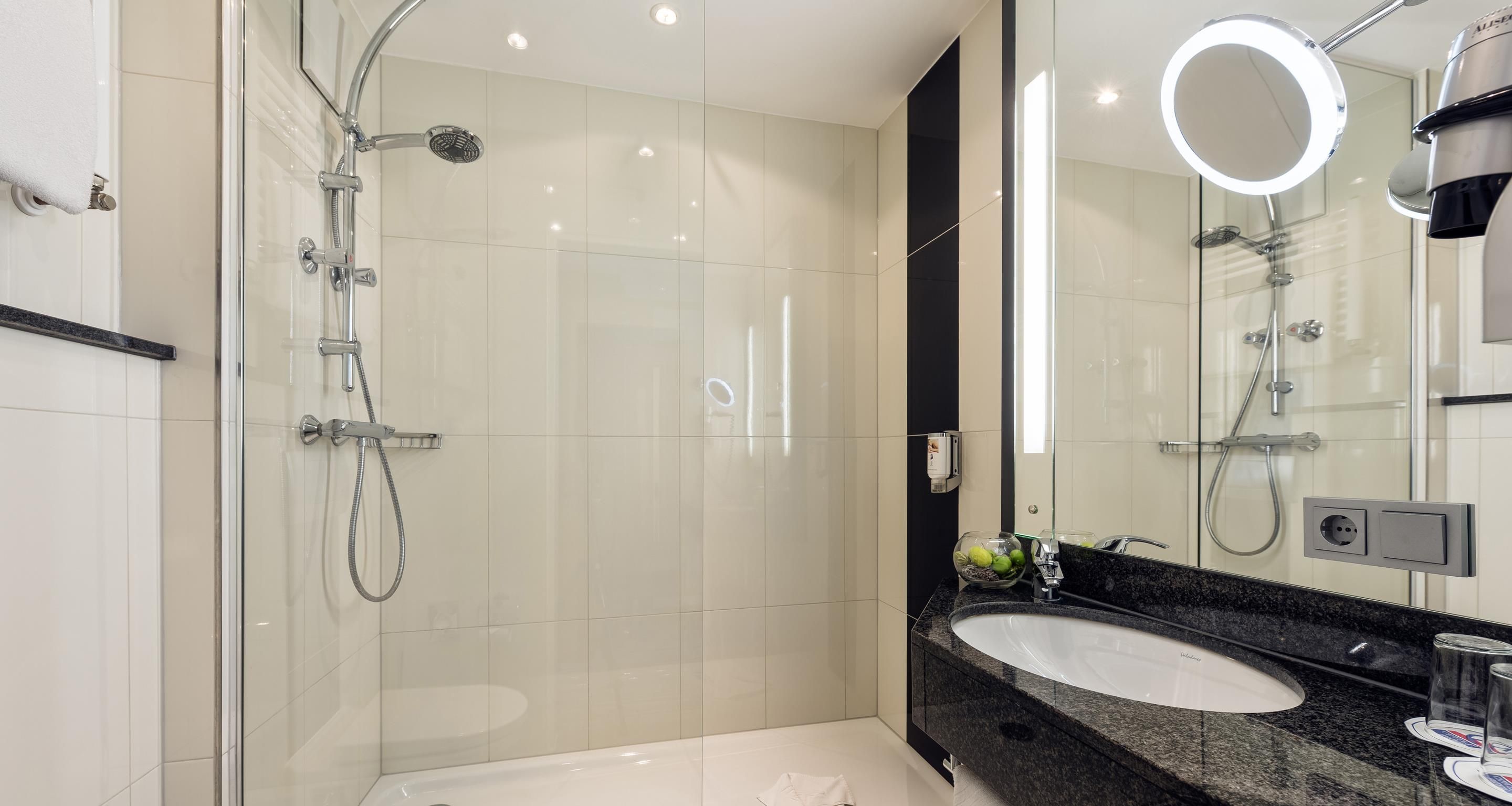 A modern bathroom with a glass-enclosed shower, a vanity with a sink, and a large mirror with integrated lighting.