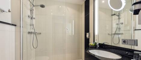 Un baño moderno con ducha envuelta en vidrio, tocador con lavabo y un espejo grande con iluminación integrada.