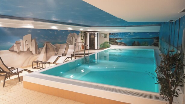An indoor swimming pool with a mural of a mountainous landscape, a slide, and lounge chairs.