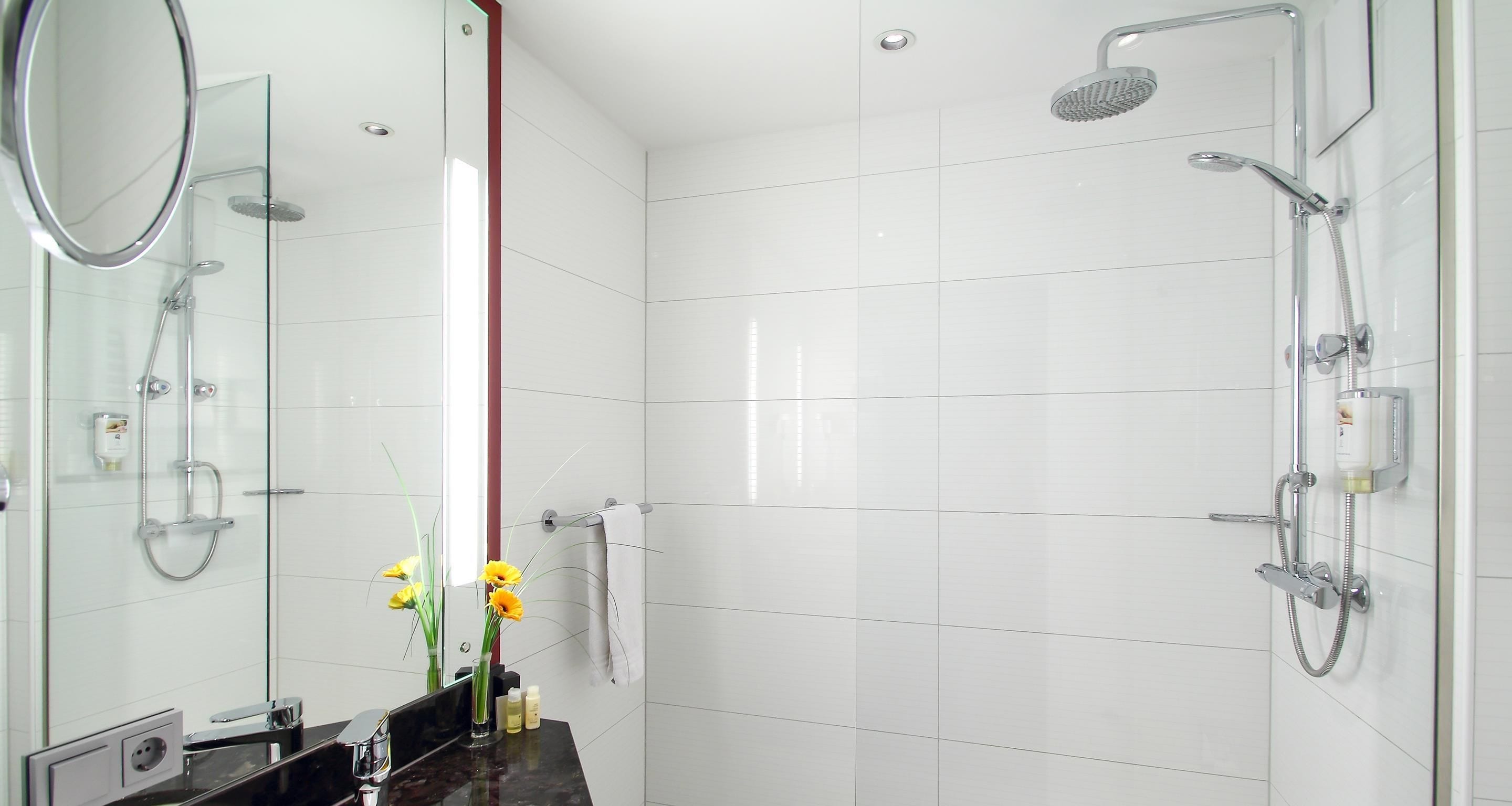 Un baño moderno con cabina de ducha de vidrio, tocador con espejo y un jarrón con flores.