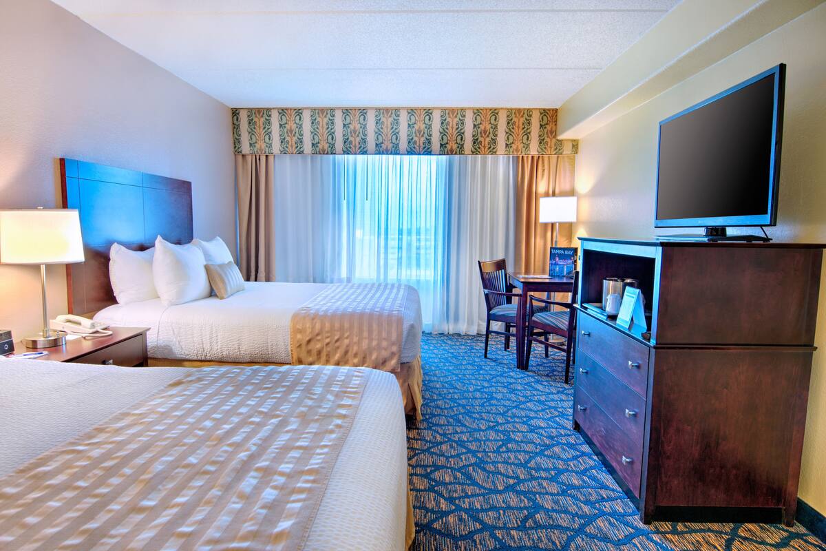 A hotel room with two beds, a television, a desk, and a dresser.
