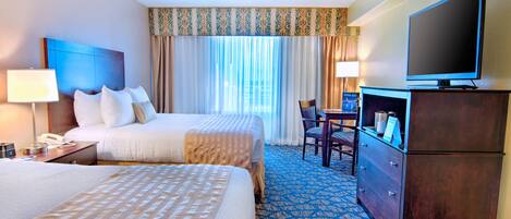 A hotel room with two beds, a television, a desk, and a dresser.