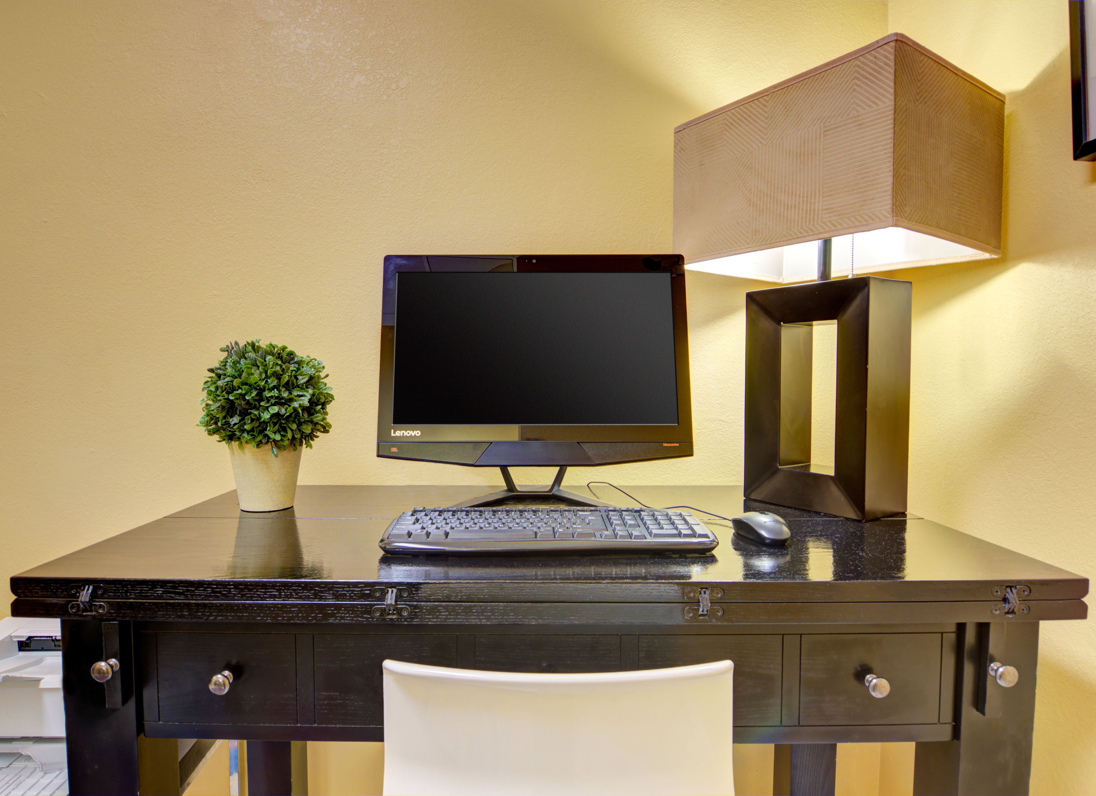 Een hotel receptie met een computer, toetsenbord, muis, lamp en een kleine plant in pot.