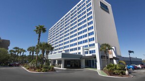 Un hotel alt i modern, amb moltes finestres, entrada coberta i un aparcament amb diversos cotxes.