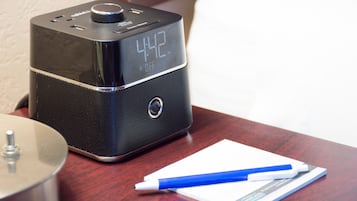 A black digital clock on a wooden table with a blue pen and a booklet.