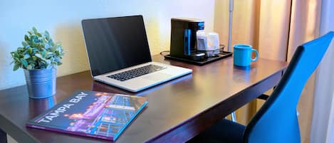 A hotel desk with a laptop, a coffee maker, a mug, a plant, and a book titled "Tampa Bay."