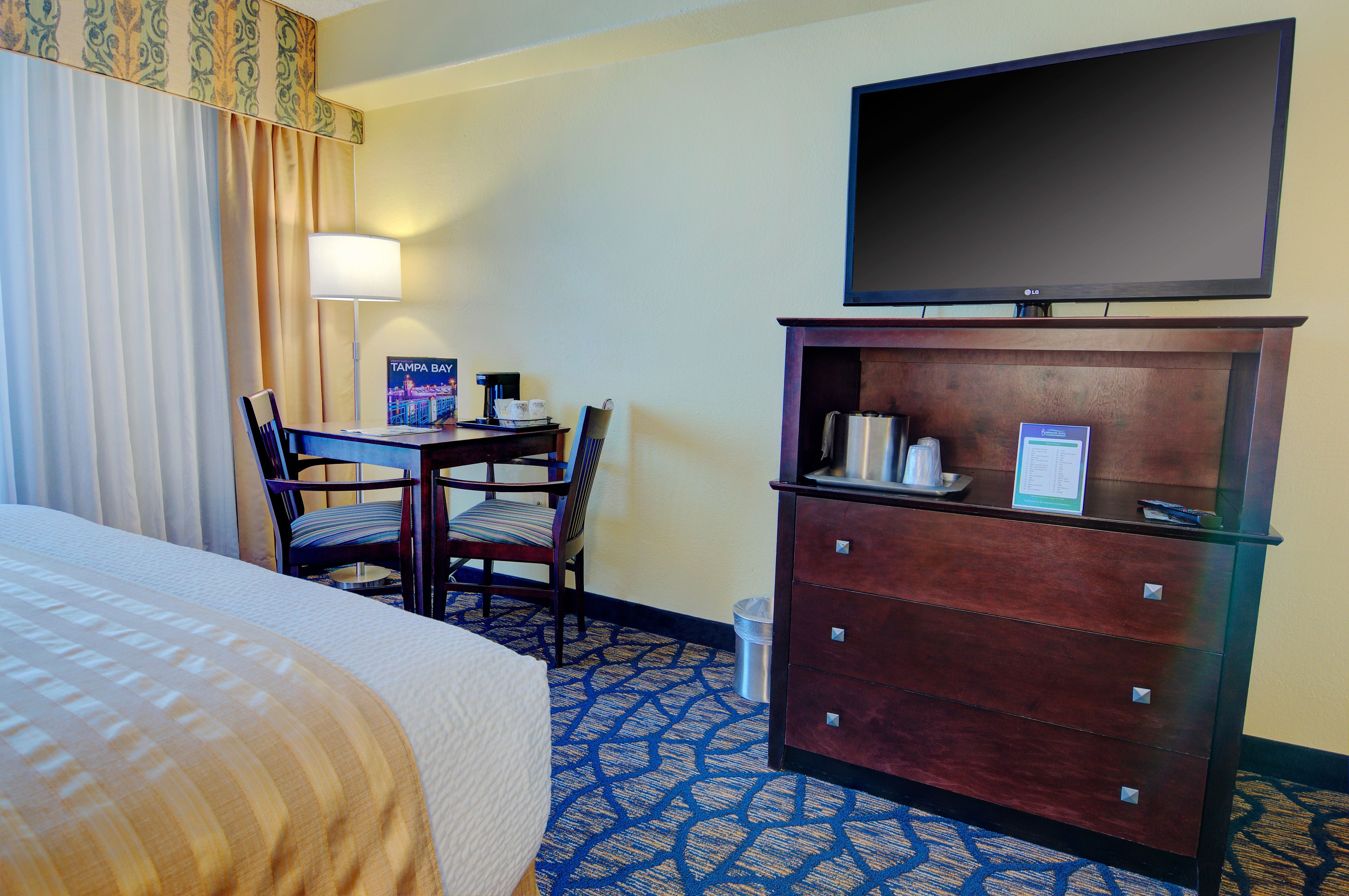 A hotel room with a bed, a desk with a chair, a television mounted on a wooden cabinet, and a patterned carpet.