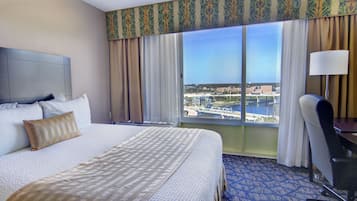 A hotel room with a large bed, a desk, and a view of a marina.