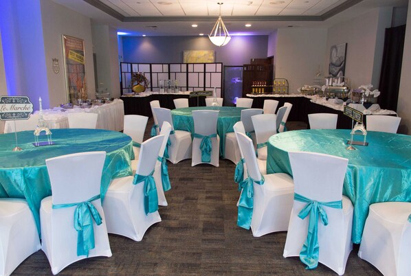 Une salle de conférence avec des tables rondes recouvertes de nappes turquoise et des chaises blanches ornées de rubans turquoise.