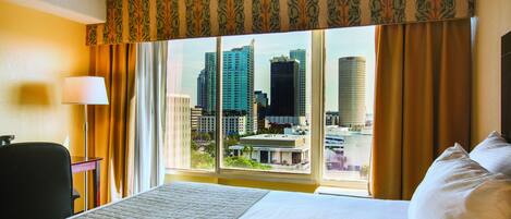 A hotel room with a large bed, a desk, and a window with a city view.