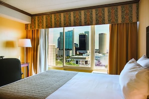 Une chambre d’hôtel avec un grand lit, un bureau et une fenêtre donnant sur la ville.