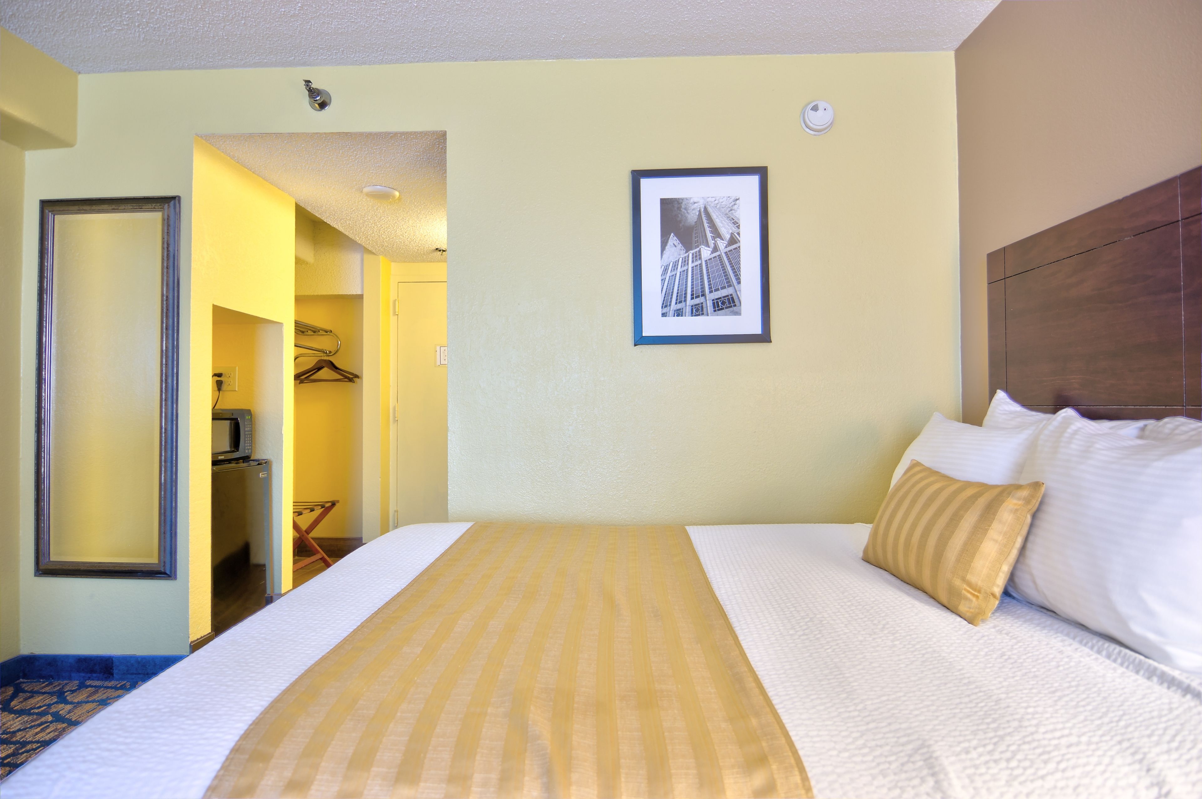 A hotel room with a bed, a framed picture on the wall, and a hallway leading to a bathroom.