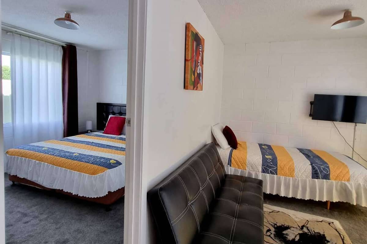 A room with two beds, a sofa, a painting, and a TV.
