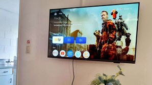 Un téléviseur à écran plat fixé au mur, affichant une affiche de film et une interface télévisuelle avec différentes icônes d’applications.