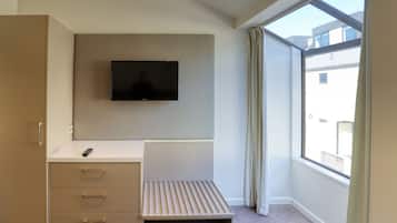 A bedroom with a bed, a TV mounted on the wall, a window, and a view of the outside.