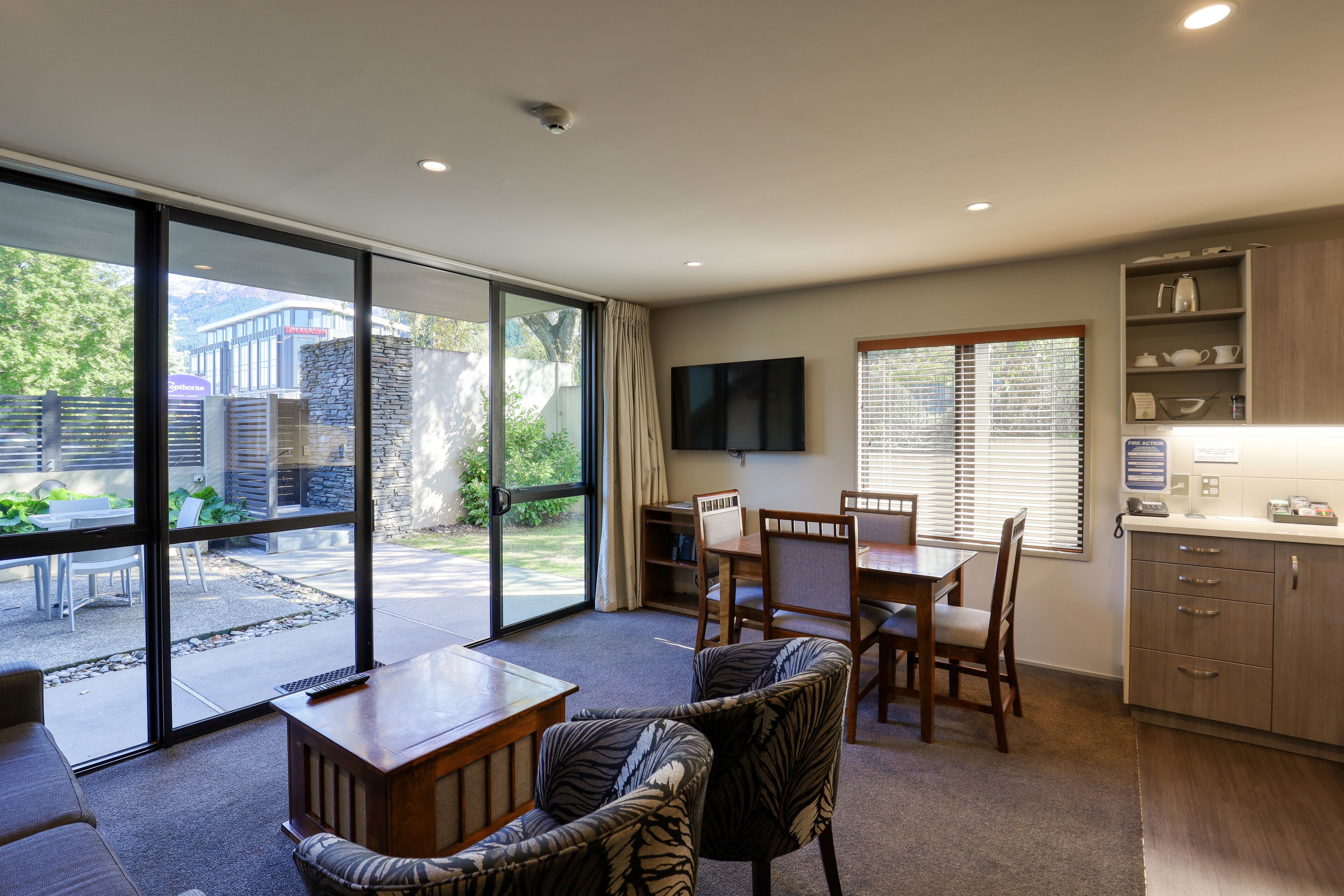 A modern kitchen with wooden cabinets, a dining area with a table and chairs, and a large sliding glass door leading to an outdoor patio.