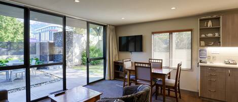 A modern kitchen with wooden cabinets, a dining area with a table and chairs, and a large sliding glass door leading to an outdoor patio.