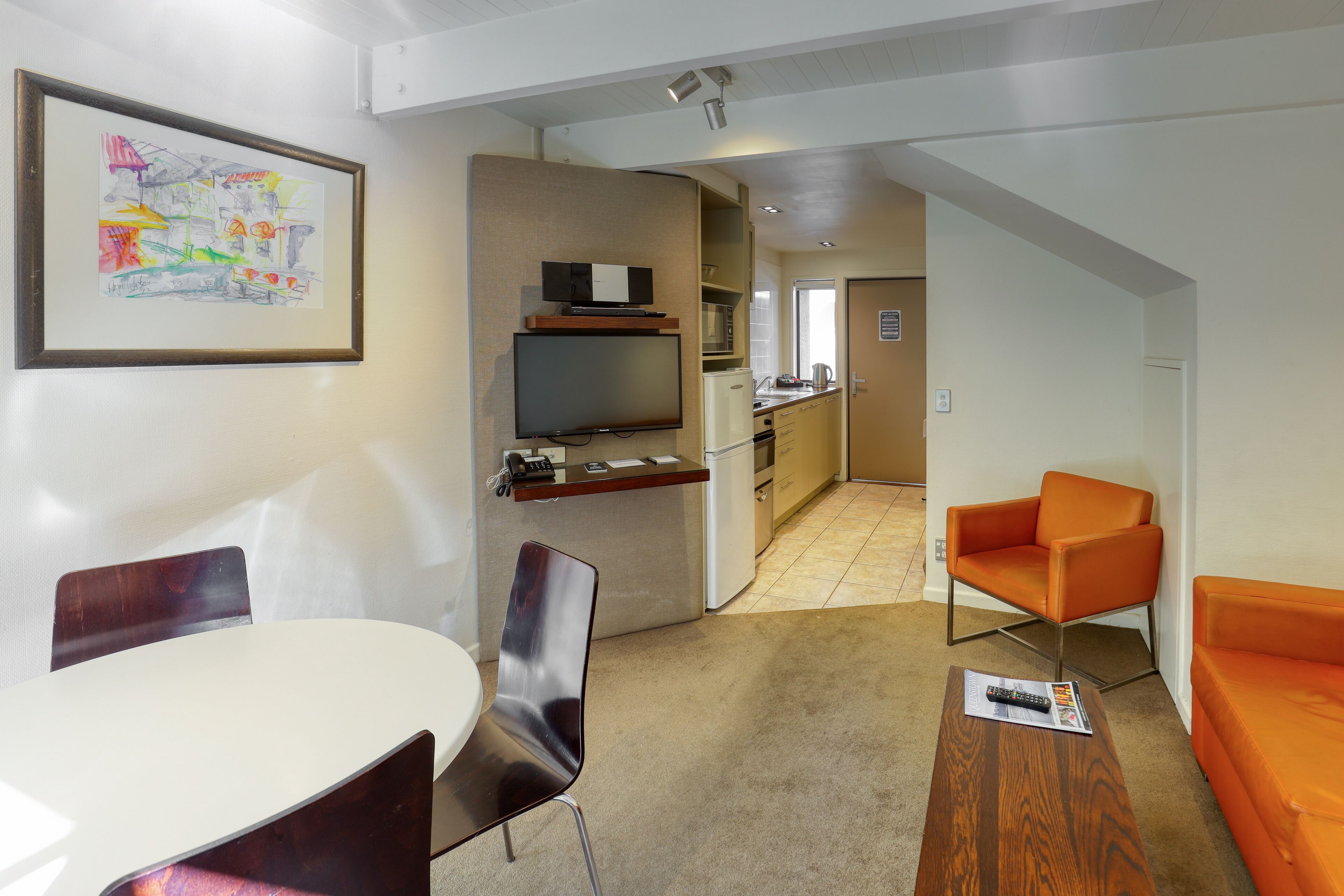 Una sala de estar moderna con una mesa de comedor, dos sillas, un sofá, un televisor y una zona de cocina al fondo.