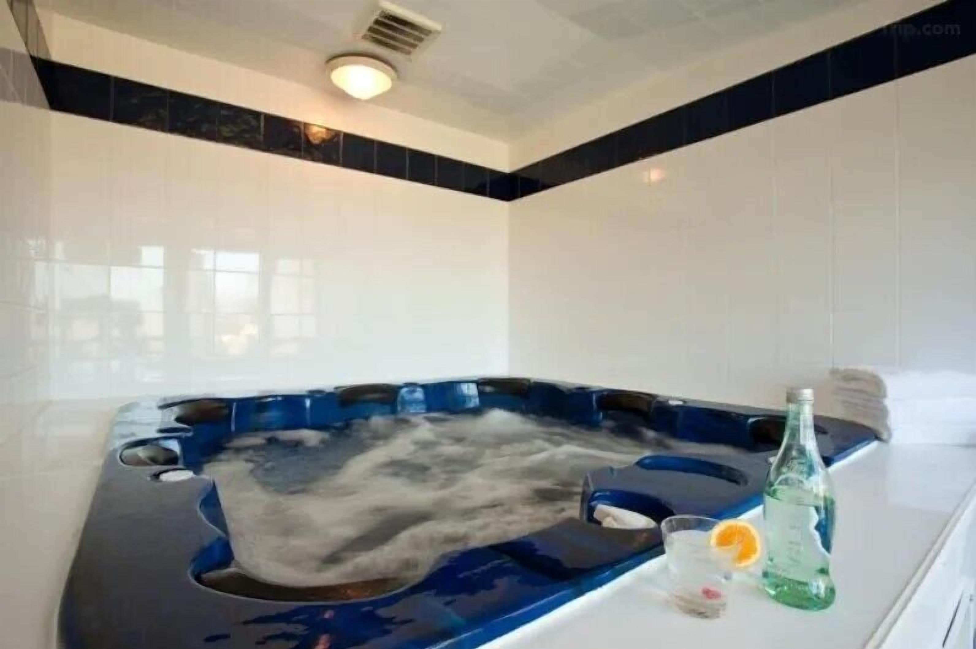 A hot tub with a blue interior, a bottle of water, and a glass with an orange slice on a white countertop.