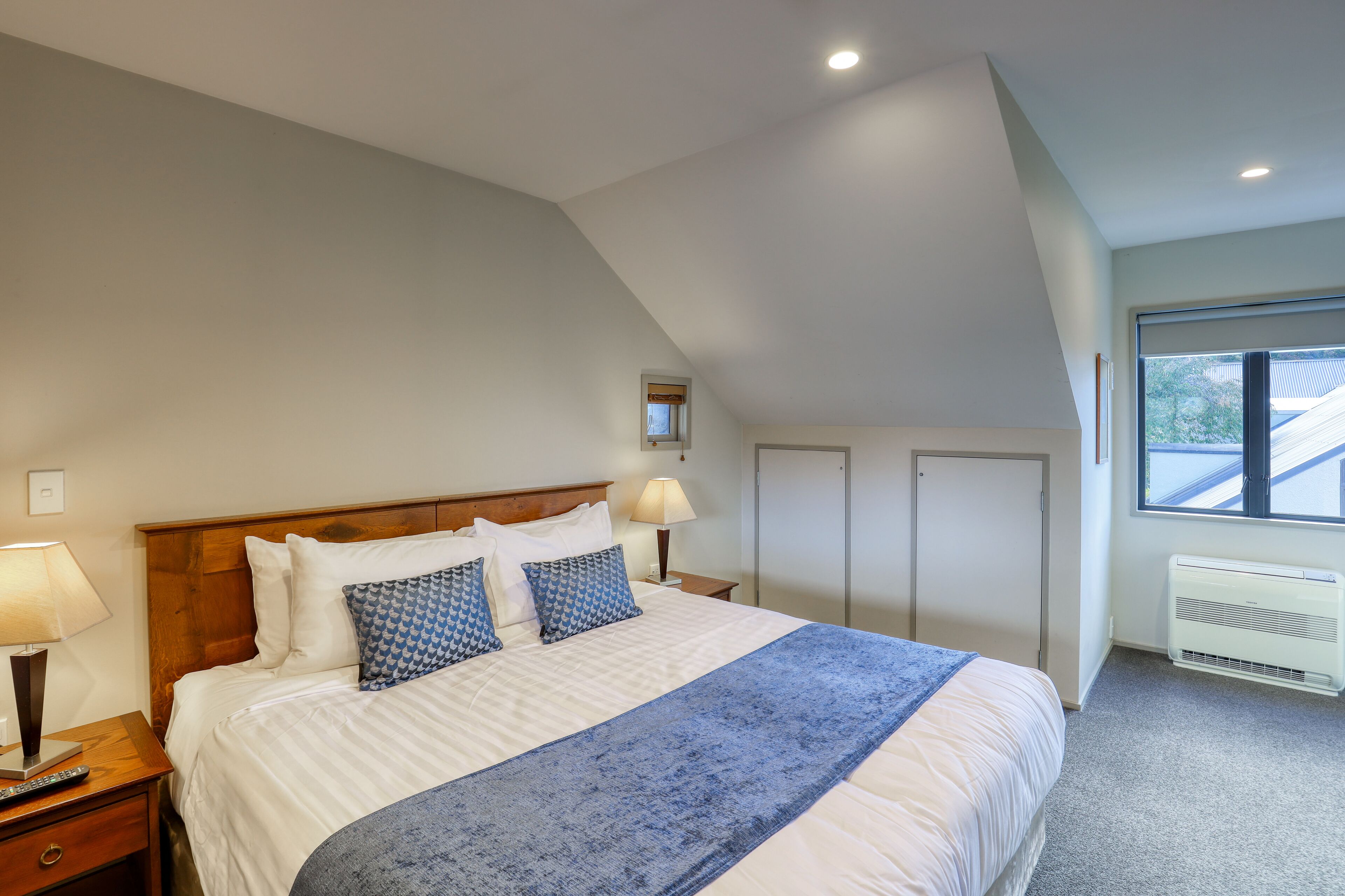 A bedroom with a large bed, two bedside tables with lamps, a window with blinds, and a ceiling fan.