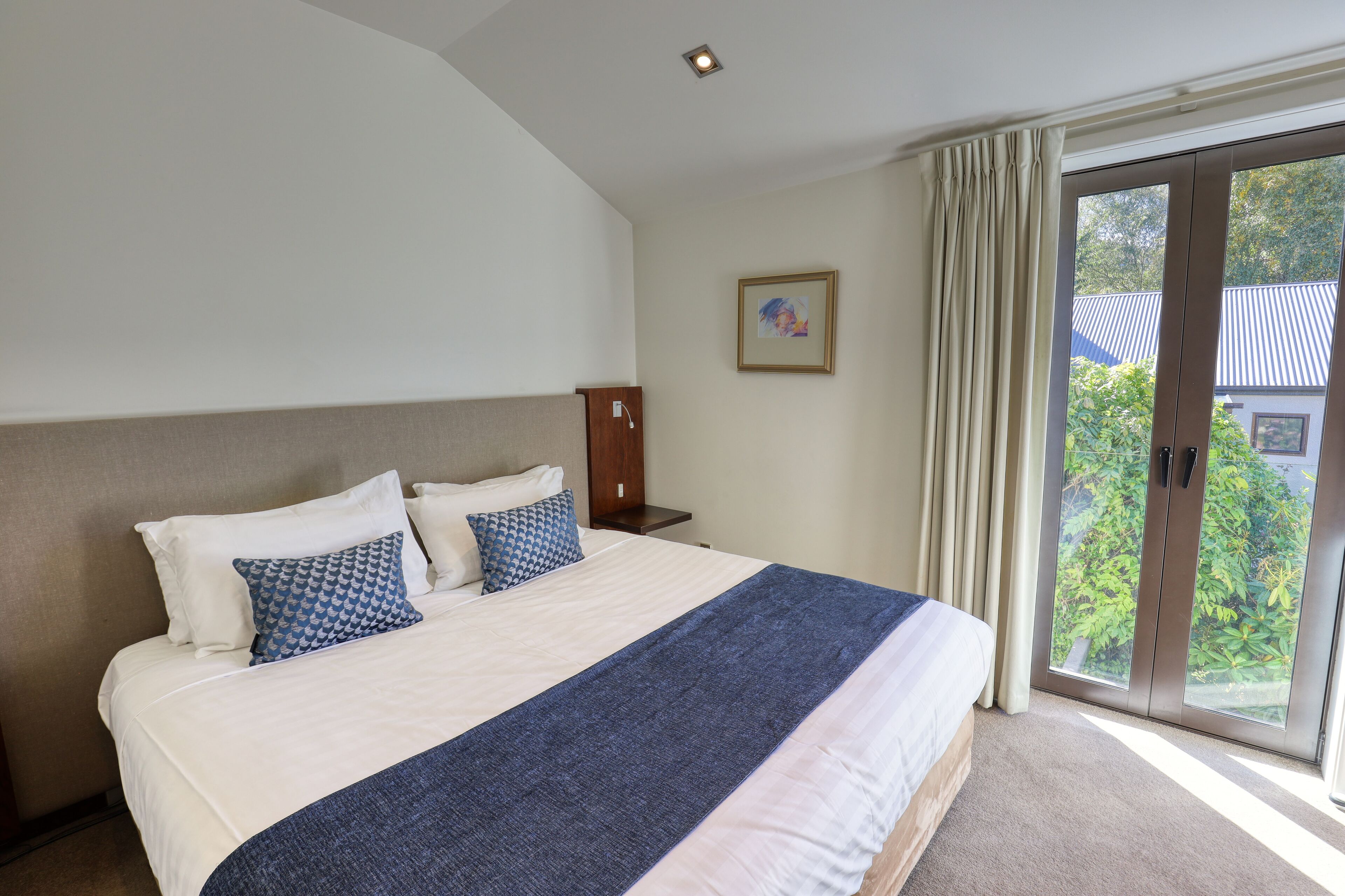 Habitación de hotel con una cama grande, una mesita de noche, un cuadro en la pared y una puerta corrediza de vidrio al exterior.