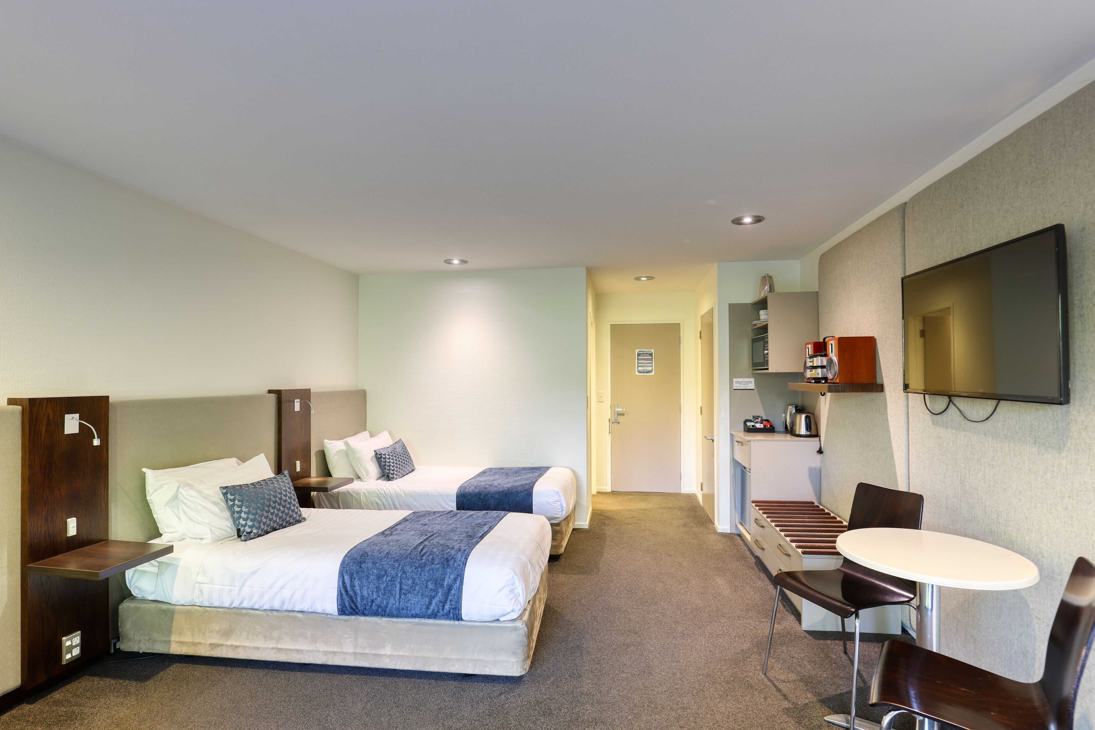 Une chambre d’hôtel avec deux lits, un bureau, une chaise, une télévision et une kitchenette.