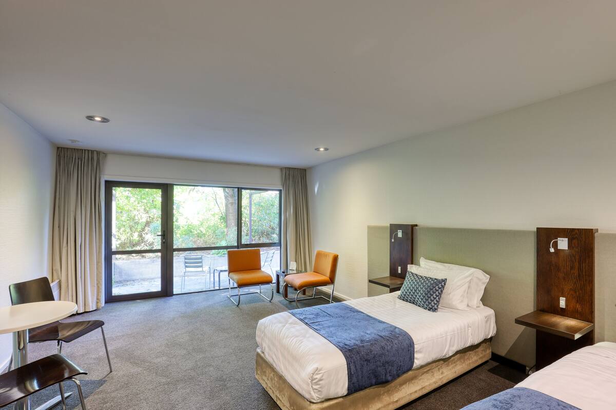 Habitación de hotel con una cama grande, dos sillones, un escritorio y vistas al exterior a través de una puerta corrediza.