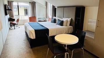 A hotel room with a bed, a desk, a chair, and a small table.