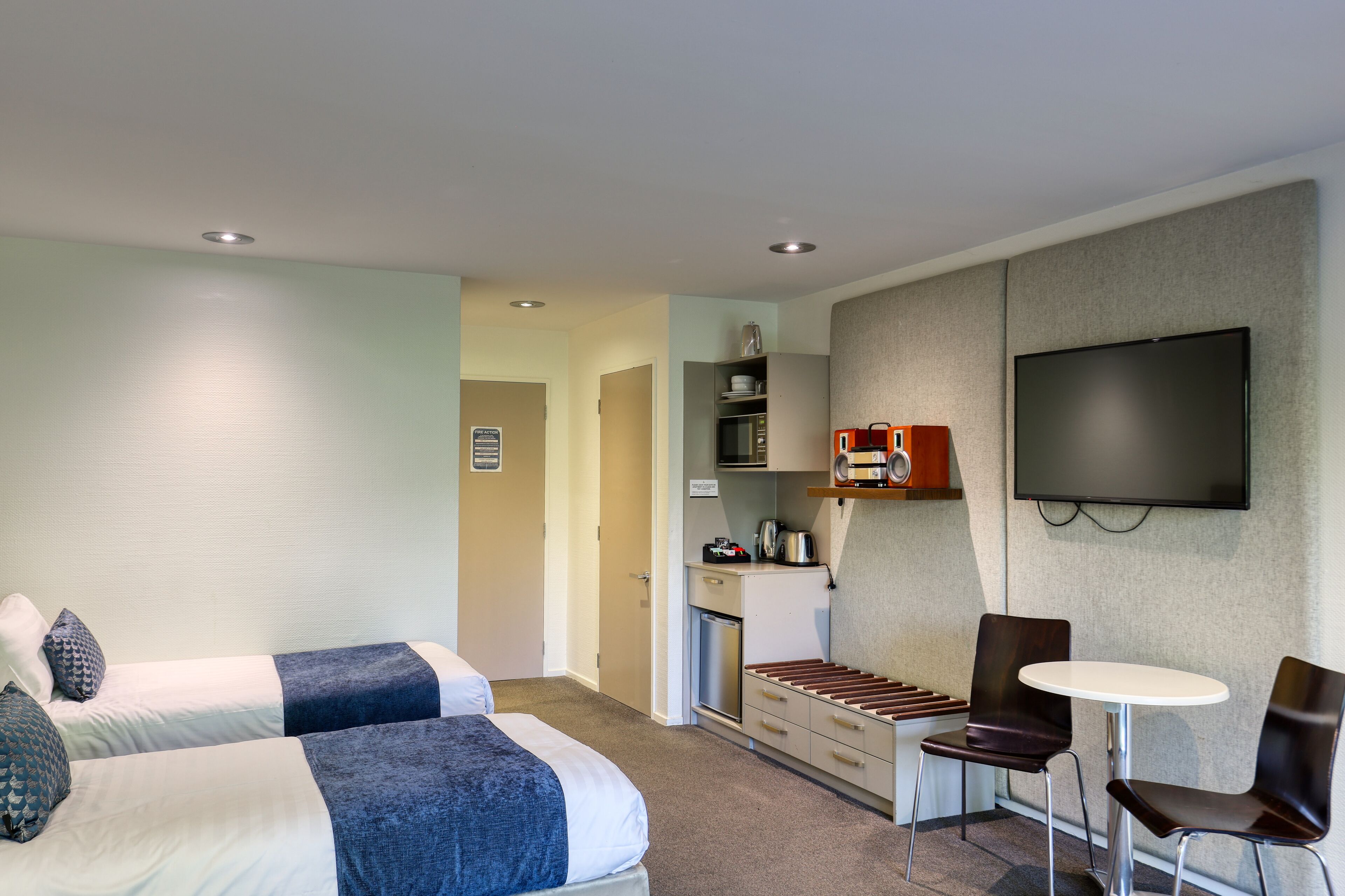Habitación de hotel con dos camas, kitchenette, televisión y una pequeña zona de comedor.