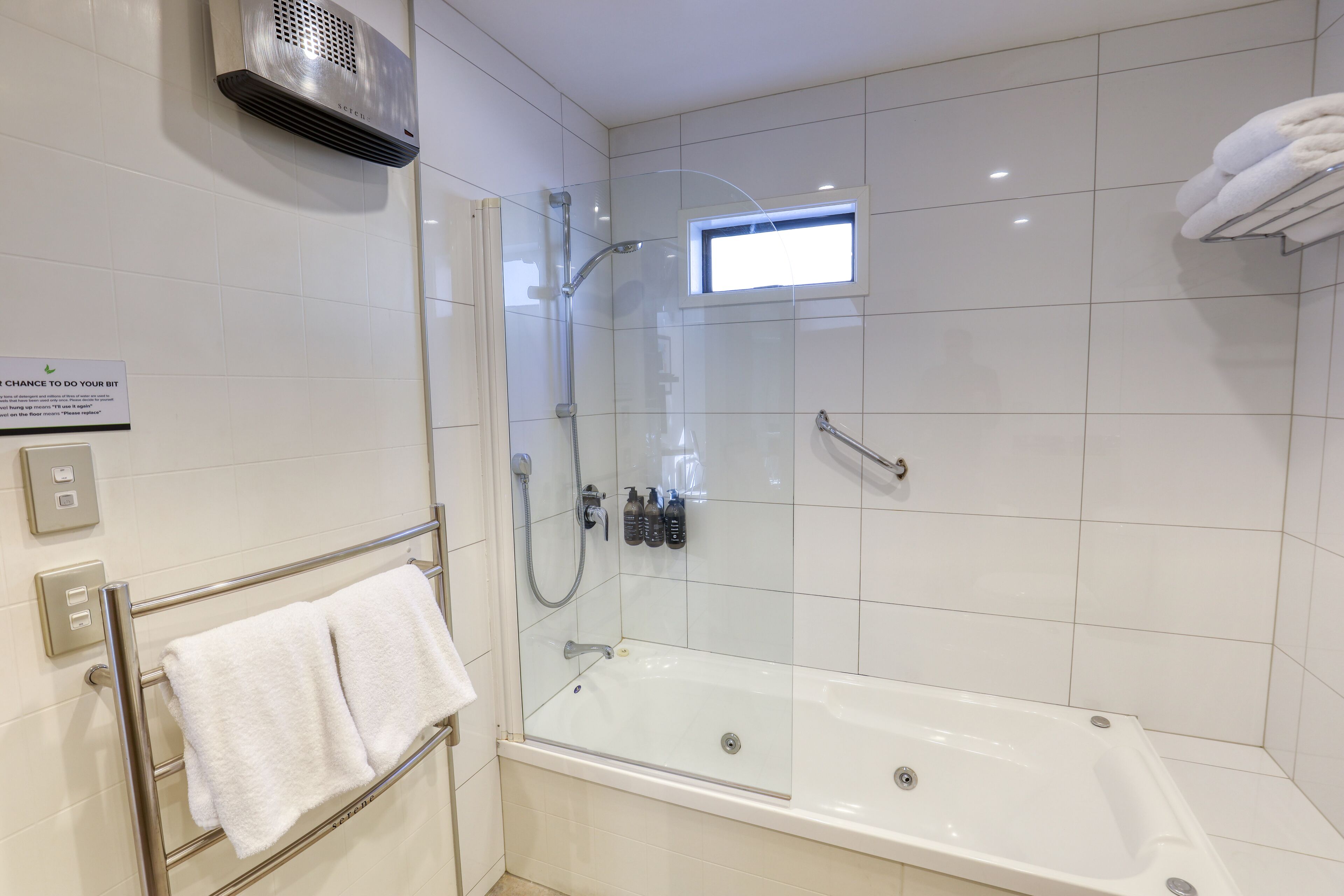 Un baño moderno con ducha envuelta en vidrio, una bañera blanca y un perchero con toallas dobladas.