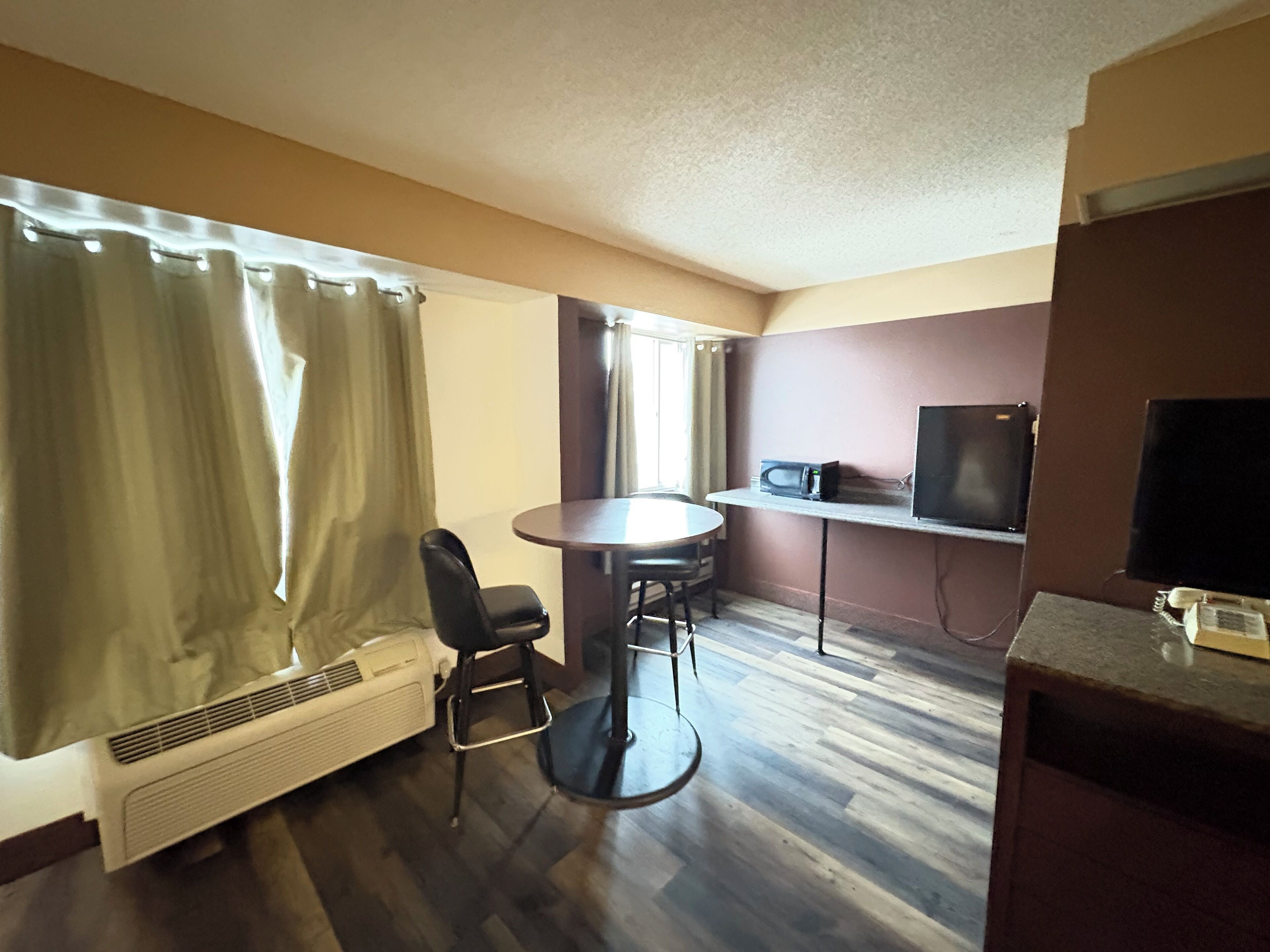Una habitación compacta con una mesa redonda, dos sillas, una kitchenette pequeña con microondas, televisor y calefacción.