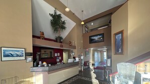 A hotel lobby with a reception desk, a large plant, a clock, and a view of the hallway.