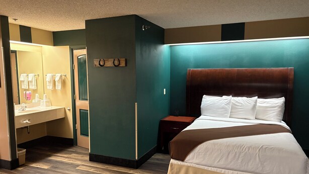 A hotel room with a bed, a vanity with a mirror, and a nightstand.