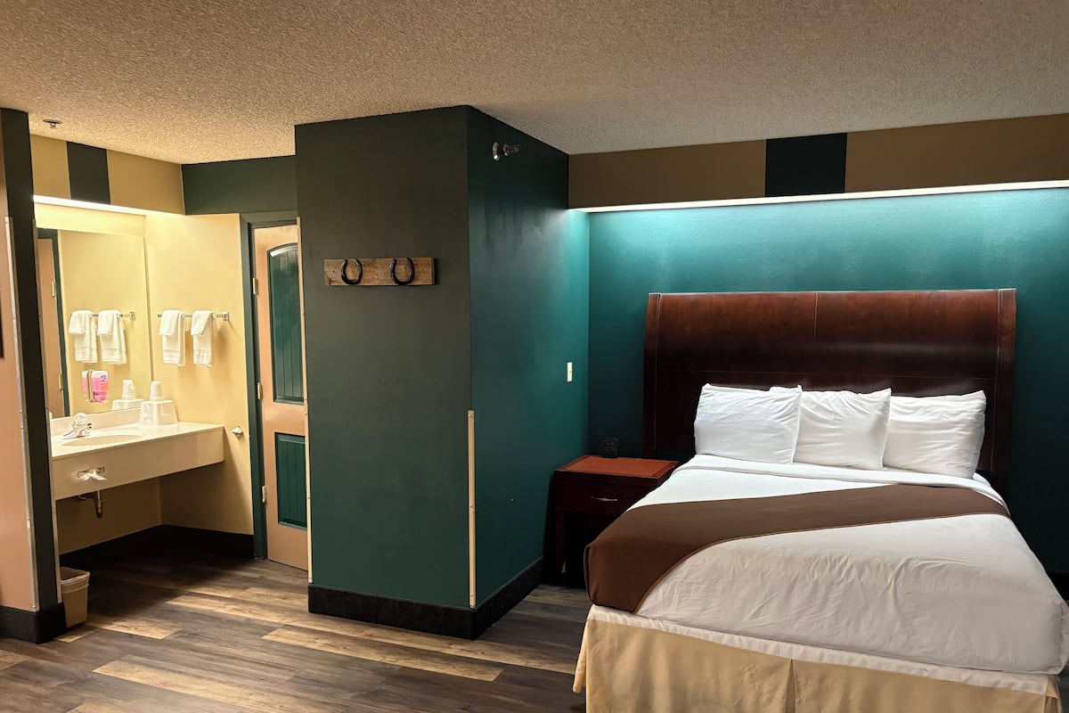 A hotel room with a bed, a vanity with a mirror, and a nightstand.