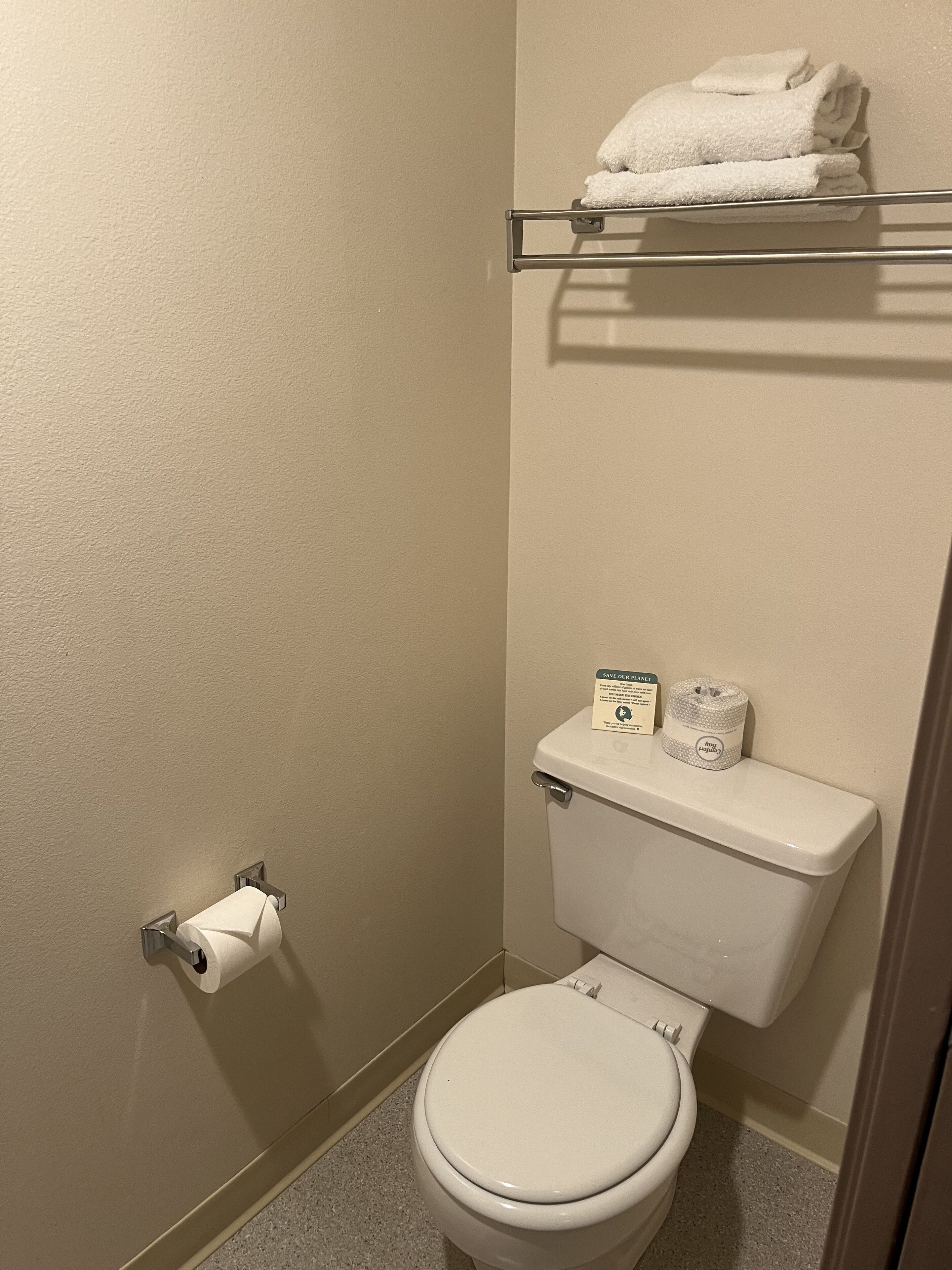 A small bathroom with a toilet, a towel rack with folded towels, a toilet paper holder, and a trash can.
