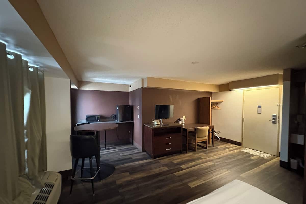A hotel room with a bed, a desk with a chair, a television, and a wardrobe.