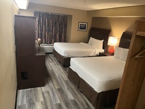 A hotel room with two beds, a small seating area, a window with curtains, and a picture on the wall.