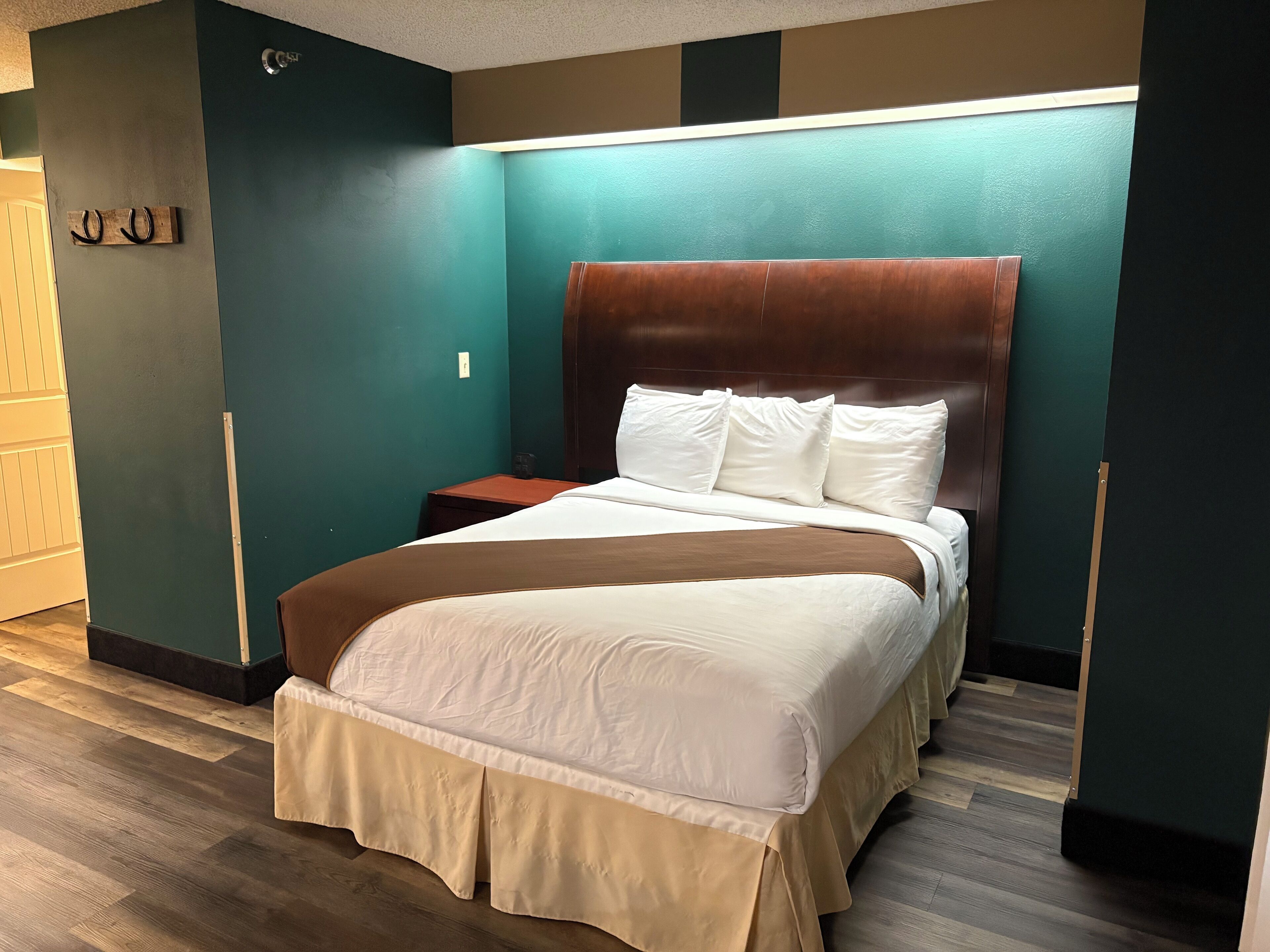 A neatly made bed with a brown headboard, a wooden nightstand, and teal walls.