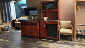 A hotel room with a wooden desk, a television, a refrigerator, a microwave, and a seating area with a sofa and chairs.