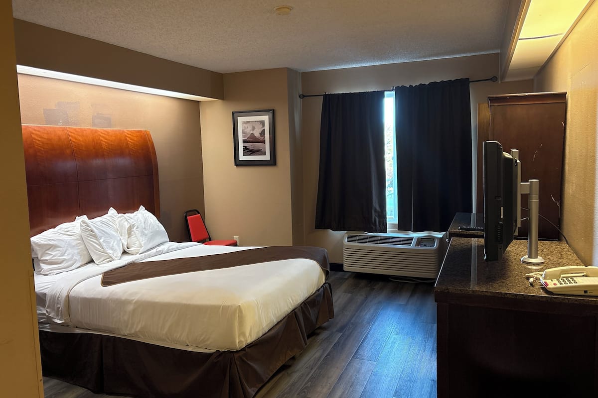 A hotel room with a bed, a desk with a telephone, a heater, and a window with curtains.