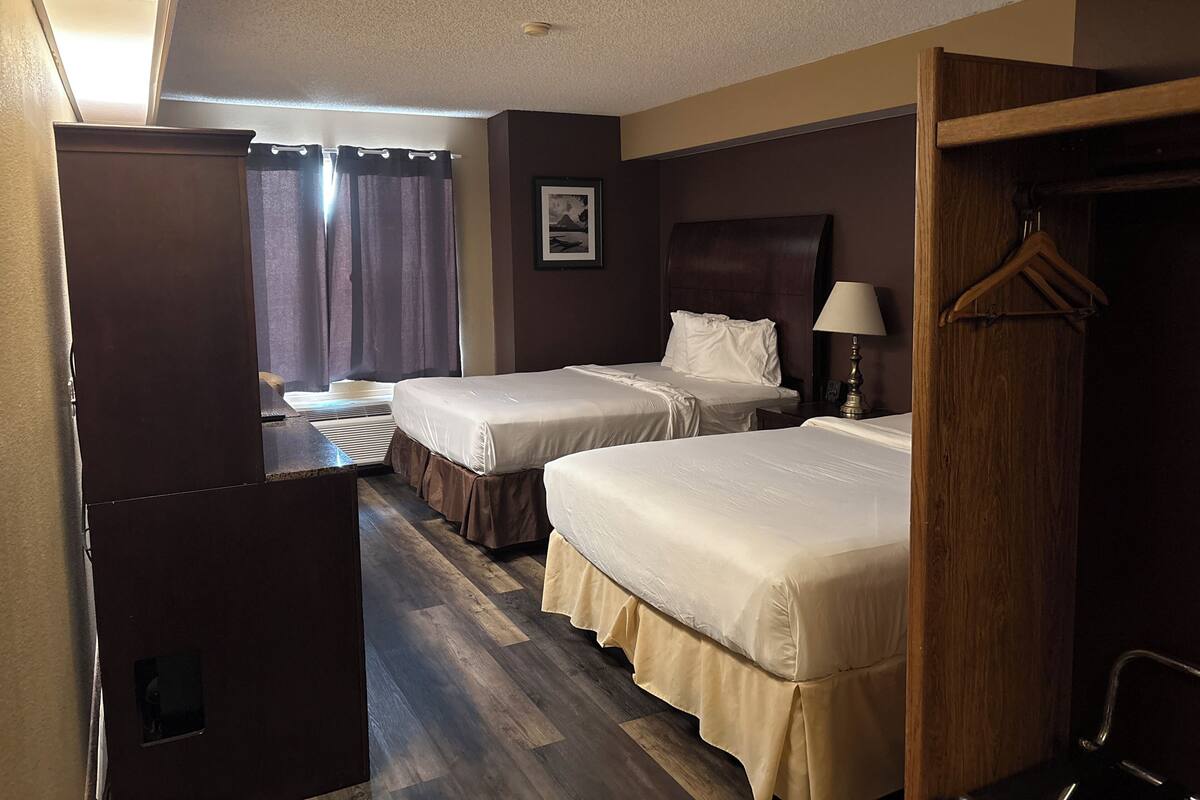 A hotel room with two beds, a desk, a chair, a wardrobe, and a picture on the wall.