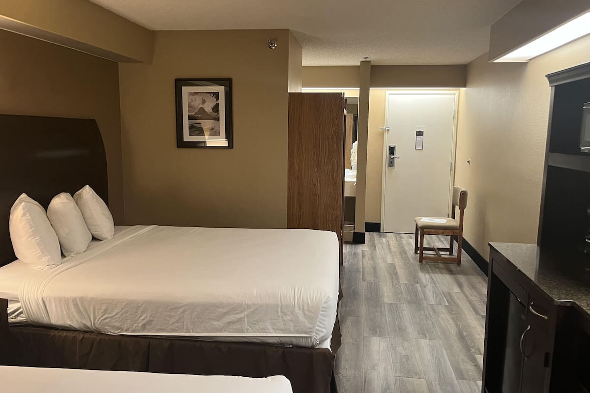 A hotel room with a large bed, a desk with a chair, a wardrobe, and a door leading to another room.